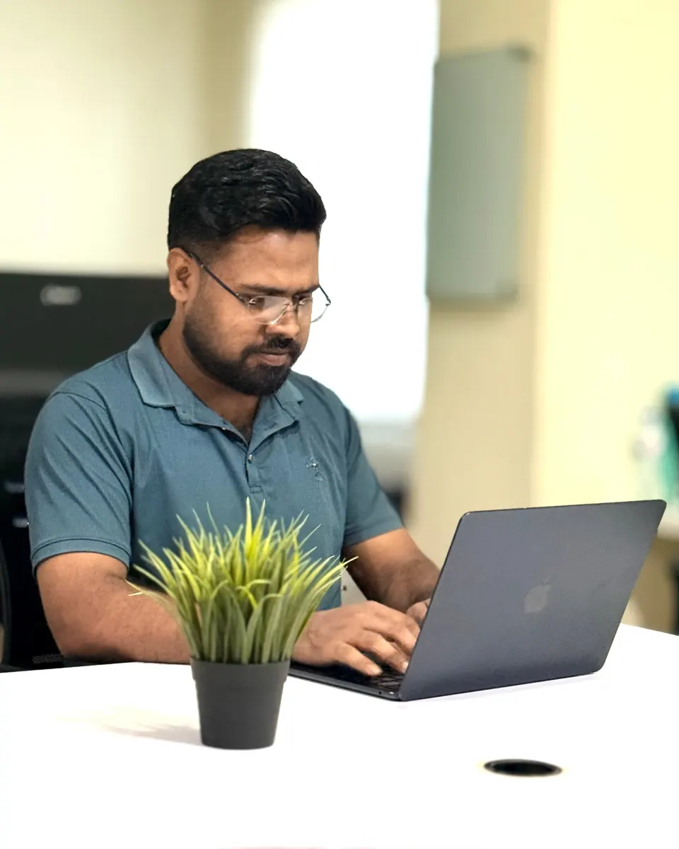KMR Jibon working on a laptop behind a small desk plant